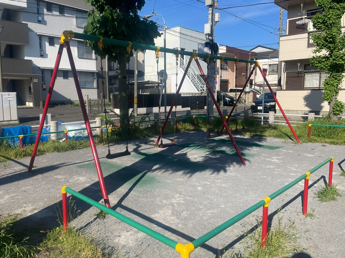 赤と緑のブランコ2連。青空のもと木陰に設置されている