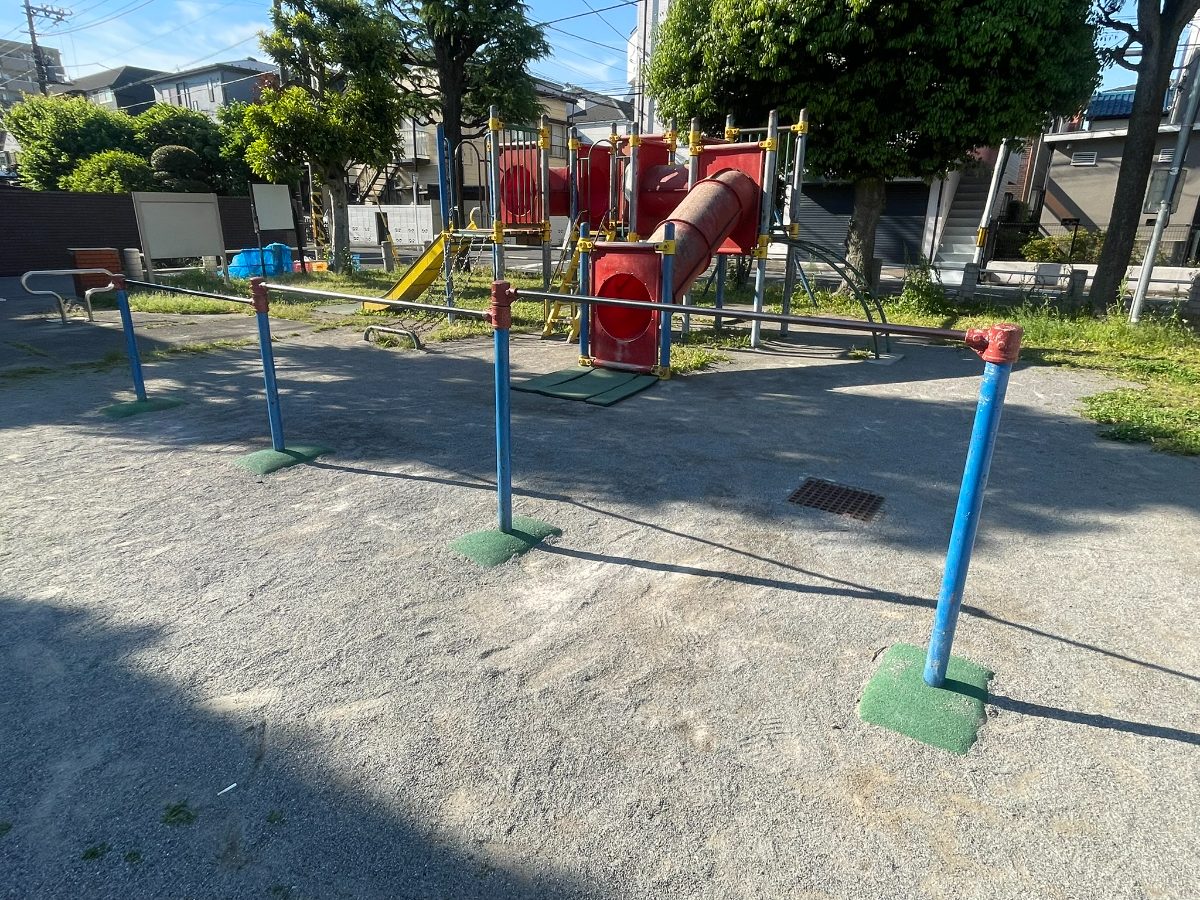 鉄棒と奥に赤い複合遊具。広い空間に配置されている