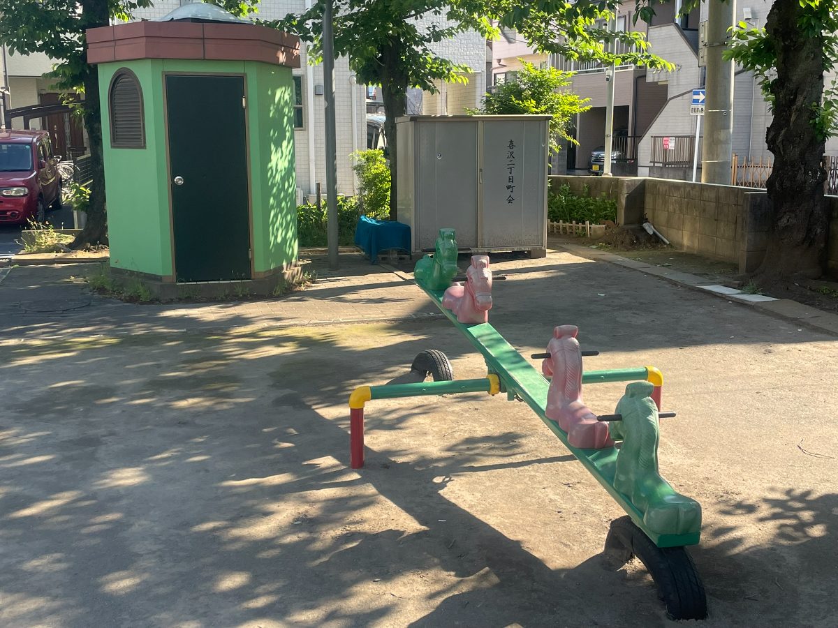 うま型ハンドルのシーソーと緑のトイレ建物。木陰の中に配置されている